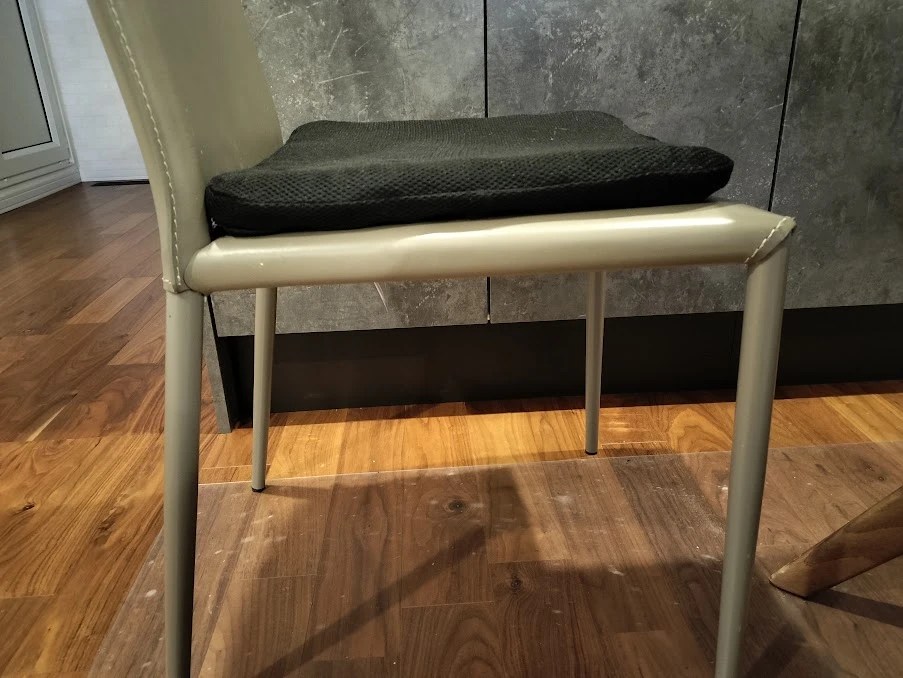 食卓の椅子に黒いクッションを敷いた所を斜め横から。クッションの厚みの分だけ座面が高くなっている